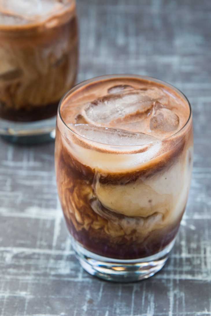 A 45 degree photograph of a glass filled with iced mocha recipe. There's a second glass out of focus in the background.
